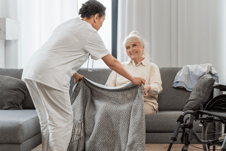 Carer arranging a blanket for a smiling elderly woman at home